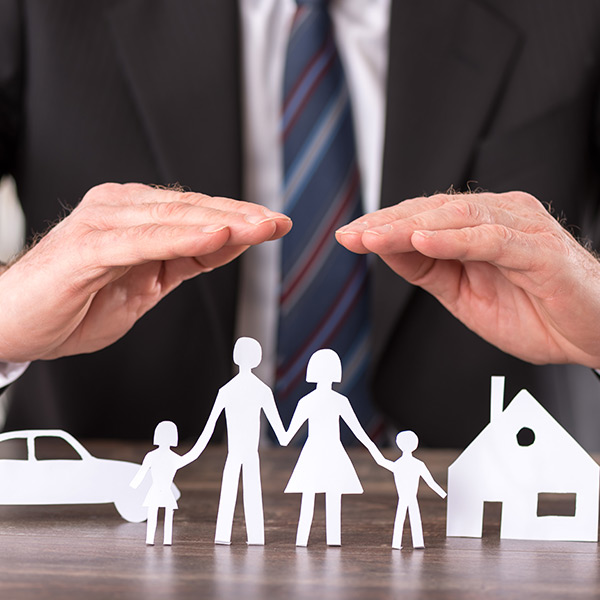 Mann hält Hände schützend über Figuren einer Familie mit Haus und Auto